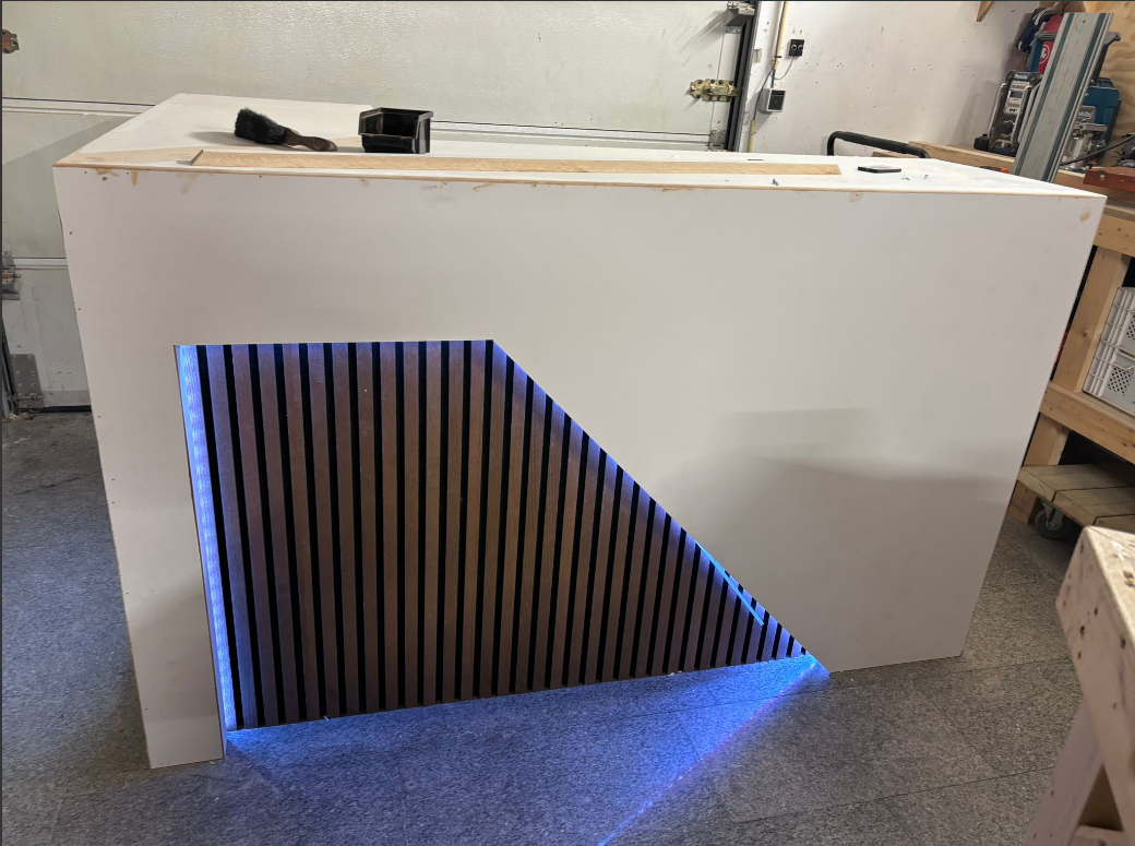 Bar met koelkast en ledverlichting. De bar is wit van kleur en is nog niet helemaal afgewerkt. De led verlichting staat aan en is blauw van kleur. De foto is genomen in de werkplaats van Haarsma Bouw & Timmerwerken.